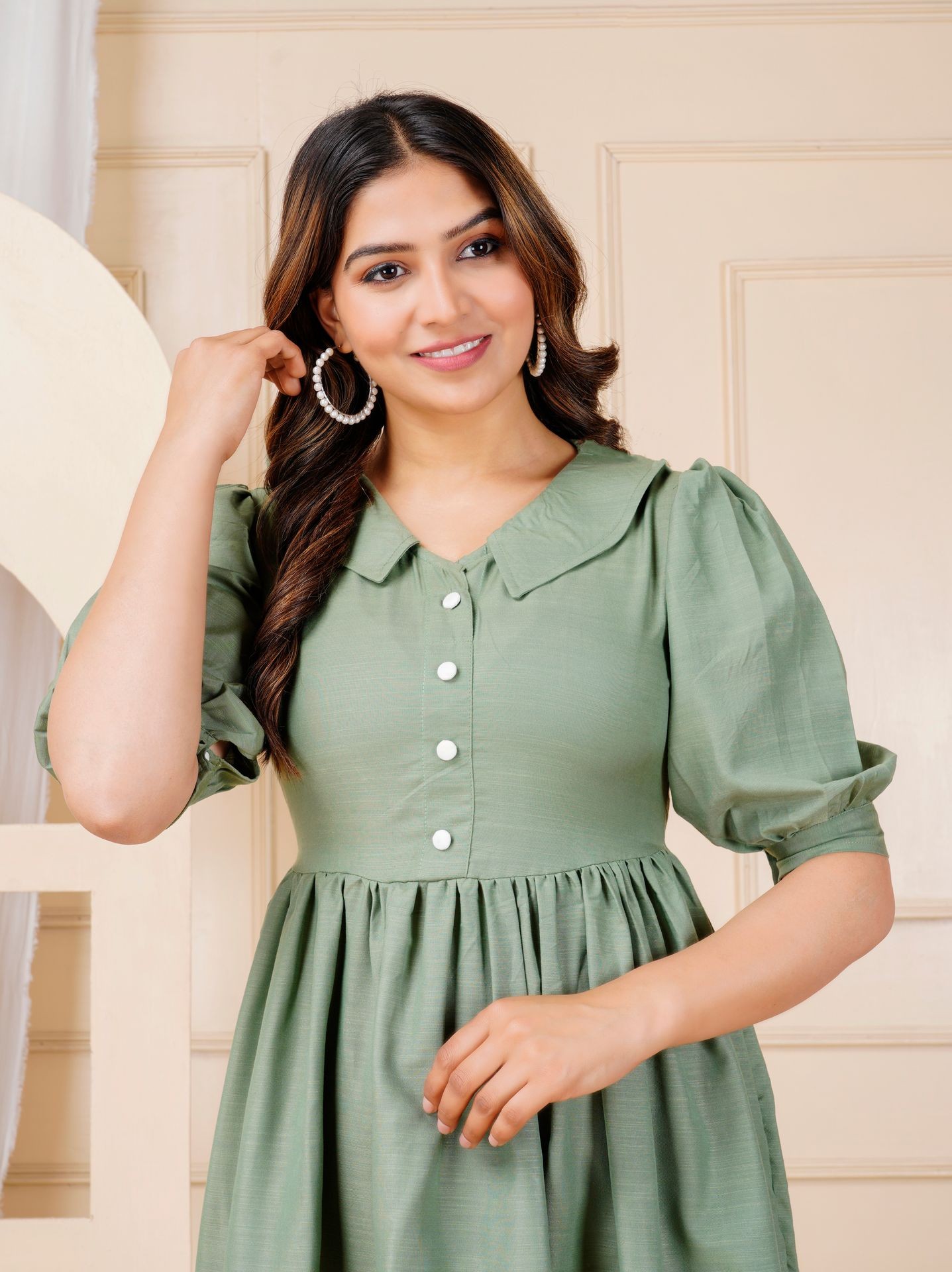 Woman in a green buttoned dress with puffed sleeves, wearing large pearl hoop earrings.